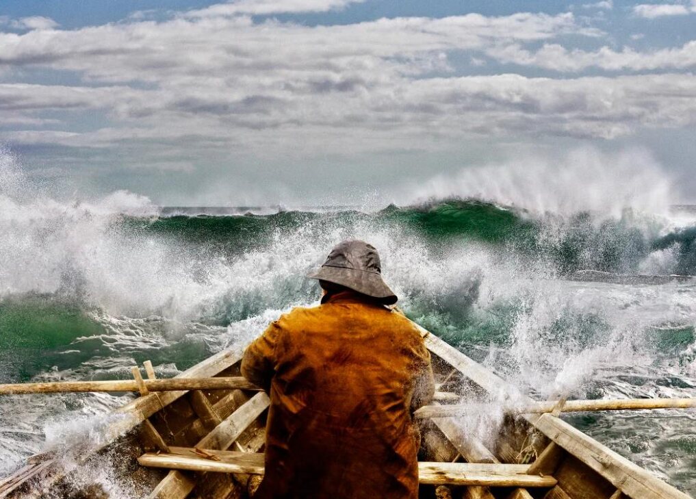 Fisher rowing a small boat into breaking waves
